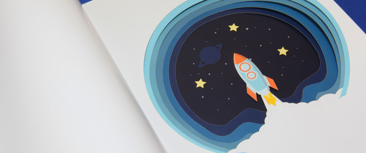 Un troquel con forma de cohete y el espacio, en el interior de un libro infantil - Troquelado laser - Truyol Digital